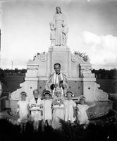 Priest and children in front of fountain, Hope Haven and Madonna Manor