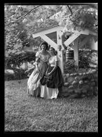 Girls wearing antebellum style dresses and standing by a "wishing well"