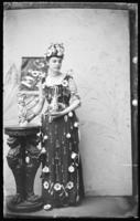 Woman with cups, saucers, silverware, and chandelier crystals hanging on costume with cupids on her shoulders.