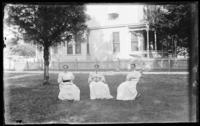 Group of 3 women sitting in chairs in yard with side of house in background.