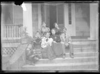 Group of man, woman, 3 young women, and 2 boys sitting on front steps of house with some holding food
