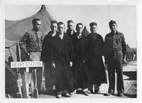 Soldier with stethoscope, five men appearing to be patients, and one soldier standing together outside tent next to HEART STATION sign