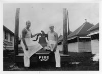 Two men dressed in white like chefs standing next to bell painted FIRE ONLY