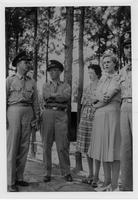Three men and two women looking serious and standing in front of pine trees