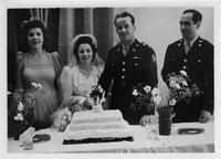 Bride with uniformed groom cutting cake with best man and maid of honor looking on