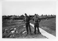 Two soldiers standing in front of rows of encampment tents