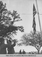 Two students watch as a flag is being raised on a flagpole in Geismer Louisiana in the 1930s