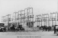 Electrical towers with cars and horse drawn wagon in foreground