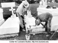 Two black men clean and whitewash family tombs in preparation for All Saints Day.